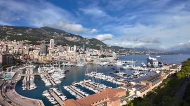 Monaco 'daki Port de Fontvieille' in yüksek açılı manzarası renkli binalar, lüks yatlar ve çevresindeki dağlık manzaraları gösteriyor.