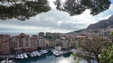 Monaco 'daki Port de Fontvieille' in yüksek açılı manzarası renkli binalar, lüks yatlar ve çevresindeki dağlık manzaraları gösteriyor.