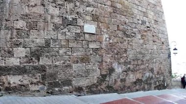 Monte Carlo, Monaco - 18 Temmuz 2025: Turistler Monako Ville 'deki yüksek ortaçağ taş kale duvarlarıyla çevrili dar, terasotta tuğlalı bir yolda yürüyorlar.