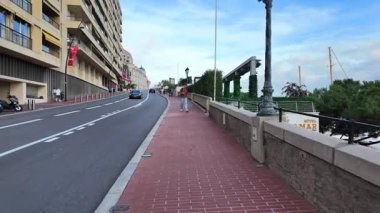 Monako Şehri, Monako - 18 Temmuz 2025: Turistler ve arabalar, güneşli bir günde Akdeniz manzarasının tadını çıkararak rıhtımdaki yayalar boyunca ilerliyorlar