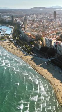 İspanya 'nın Alicante kentindeki plajda gün ışığında rahatlayan insanların bulunduğu kıyı şeridi boyunca giden arabaların insansız hava aracı görüntüsü. Dikey