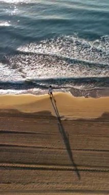 İspanya, Alicante 'de kıyıya vuran dalgalarla sahilde yürüyen adam. Dikey