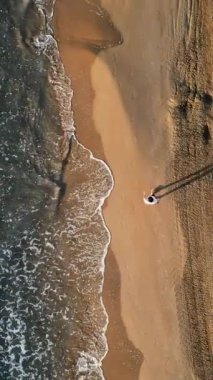 İspanya, Alicante 'de kıyıya vuran dalgalarla sahilde yürüyen adam. Dikey