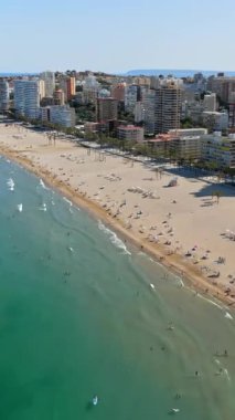 İspanya 'nın Benidorm plajında gün ışığında dinlenen insanların bulunduğu kıyı şeridi boyunca binaların insansız hava aracı görüntüsü. Dikey
