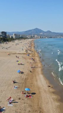 İspanya 'nın Benidorm plajında gün ışığında dinlenen insanların bulunduğu kıyı şeridi boyunca binaların insansız hava aracı görüntüsü. Dikey