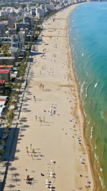 İspanya 'nın Benidorm plajında gün ışığında dinlenen insanların bulunduğu kıyı şeridi boyunca binaların insansız hava aracı görüntüsü. Dikey
