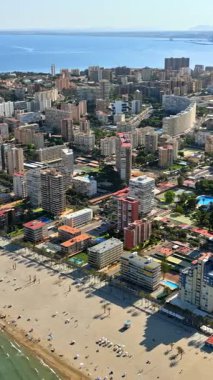 İspanya 'nın Alicante kentindeki plajda gün ışığında dinlenen insanların bulunduğu sahil boyundaki binaların insansız hava aracı görüntüsü. Dikey