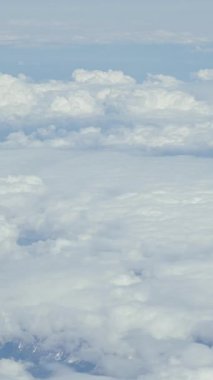 Bir uçak penceresinden beyaz, kabarık bulutların hava görüntüsü. Dikey