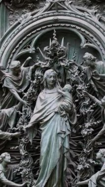 İtalya 'nın başkenti Milano' da, Duomo 'da birden fazla melek tarafından çevrelenmiş, bebek İsa' yı tutan Bakire Meryem 'in detaylı bir yardım heykelini kapatın. Dikey