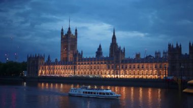 Geceleri Westminster Sarayı 'nın Thames Nehri' ne yansıyan ışıkları ve İngiltere, Londra 'dan geçen bir gezi teknesiyle manzarası.