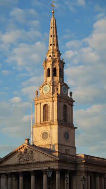 İngiltere, Londra 'da parçalı bulutlu bir gökyüzü altında yakalanan St. Martin-in-the-Fields kilisesinin uzun saat kulesi. Dikey