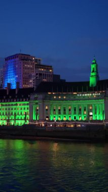 Belediye binasının manzarası akşam vakti yeşil, mavi ve pembeyle aydınlanıyor. Dikey, Londra
