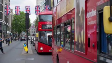 Londra, İngiltere - 12 Mayıs 2025: Klasik kırmızı çift katlı otobüsler, arabalar ve Union Jack bayrakları altında sokaklarda hareket eden insanlar