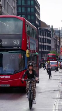 Londra, İngiltere - 12 Mayıs 2025: Kırmızı otobüsler, otobüs durağındaki yayalar ve geleneksel şehir binaları ile dolu bir cadde. Dikey