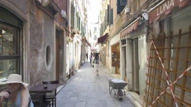 Venedik, İtalya - 9 Temmuz 2025: Turistler şehrin dar sokaklarında gün ışığında farklı butiklerin yanında yürüyorlar