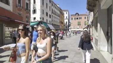 Venedik, İtalya - 9 Temmuz 2025: Turistler şehrin dar sokaklarında gün ışığında farklı butiklerin yanında yürüyorlar