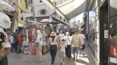 Venedik, İtalya - 9 Temmuz 2025: Turistler şehrin dar sokaklarında gün ışığında farklı butiklerin yanında yürüyorlar