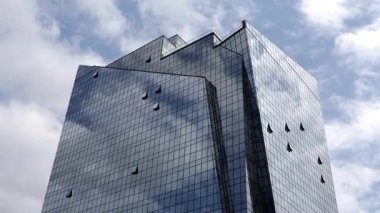 Aynalı bir ofis kulesinin alçak açılı görüntüsü ızgara cephesinde hareket eden bulutları yansıtıyor