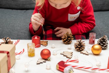 Christmas kids craft activities at home. Little child painting pine cones and wooden Christmas tree decorations at home. Holiday DIY concept for children.