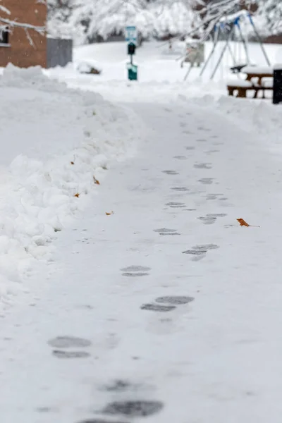 Snow on the sidewalk leading to the house and playground in the yard. Snowy road with footsteps in winter.