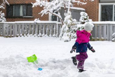 Little child playing with snow and showel outside near house in winter. Wintertime fun outdoor activities for children.