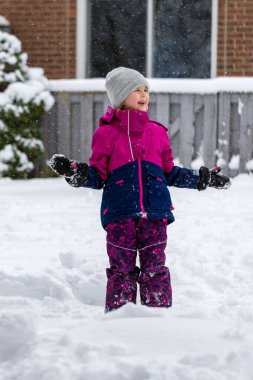 Happy smiling child playing with snow outdoors near house in winter. Wintertime fun outdoor activities for children. Snowy weather