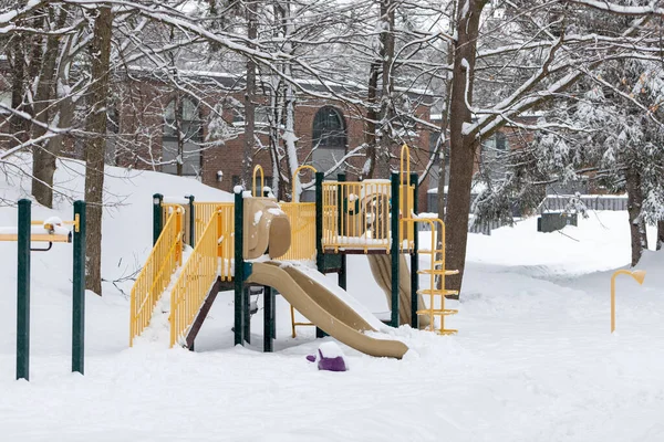 Playground with slide in park without people in residential area, covered with snow in winter season