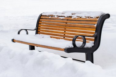 Bench covered with snow in city park. Snowfall in winter.