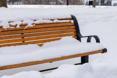 Bench covered with snow in city park. Snowfall in winter season. Cold weather conditions.
