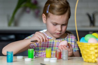 Evde oturan küçük çocuk paskalya yumurtalarını boyuyor. Tatil zanaatı yapan kız.