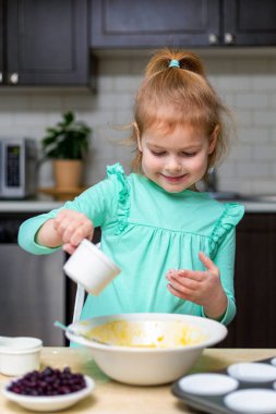 Küçük gülümseyen kız mutfakta para kazanıyor. Küçük mutlu çocuk yemekleri. Çocuk böğürtlenli ev yapımı kek yapıyor, yemek yapmayı öğreniyor..