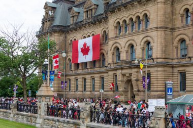 Kanada, Ottawa - 1 Temmuz 2022 Kanada Günü. Parlamento Tepesi yakınlarında kırmızı elbiseli ve bayraklı insanlar. Kanada bayrağı inşaatta.
