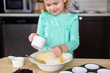 Küçük gülümseyen kız mutfakta para kazanıyor. Küçük mutlu çocuk yemekleri. Çocuk böğürtlenli ev yapımı kek yapıyor, yemek yapmayı öğreniyor..