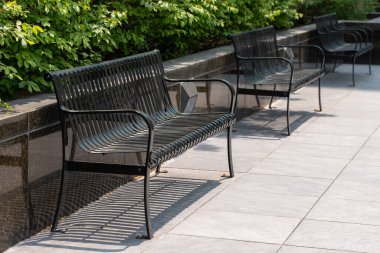 Güneşli bir yaz gününde, parkta siyah metal banklar.