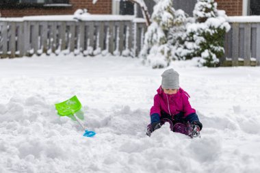 Küçük çocuk kışın evin yanında kar ve kürekle oynuyor. Çocuklar için kış eğlencesi açık hava aktiviteleri.