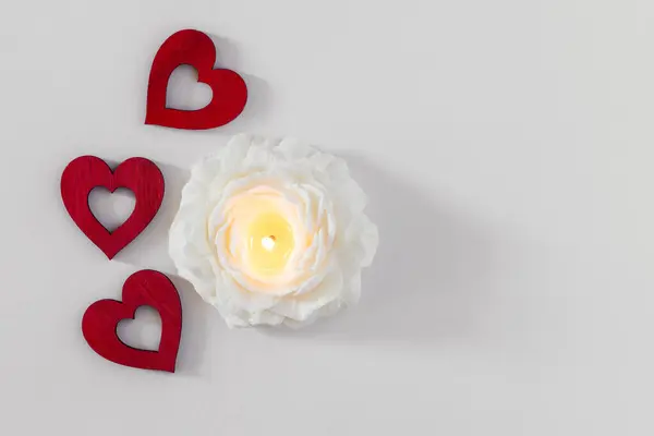 Red hearts and candle in flower shape on white background. Valentine day and love concept. Top view with copy space for text.