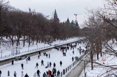Ottawa, Kanada - 8 Şubat 2025: İnsanlar kışın Rideau Kanalı 'nda paten kayıyor. Şehir merkezindeki parlamento binası.