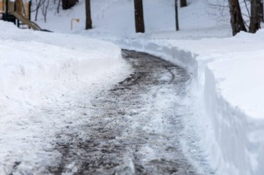 Parkta tuzlu ve eriyen karlı kış yolu.