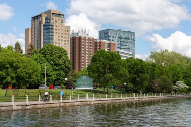 Ottawa, Kanada - 16 Mayıs 2024: Rideau Kanalı ve bisiklet yolu ilkbaharda kıyı şeridi boyunca. Yürüyen ve bisiklete binen insanların olduğu bir park..