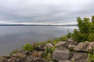 Kayalıkları ve bulutlu gökyüzü olan nehir kıyısı. Yazın deniz manzarası ve ufuk çizgisi.