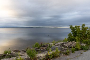 Kayalıkları ve bulutlu gökyüzü olan nehir kıyısı. Yazın deniz manzarası ve ufuk çizgisi.