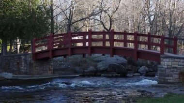 Baharda parkta bir derenin üzerinde küçük kırmızı bir köprü. Stewart Park Perth, Ontario, Kanada.