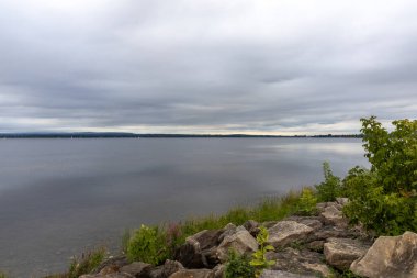 Kayalar ve bulutlu gökyüzü ile Rocky Nehri kıyısı. Yazın deniz manzarası ve ufuk çizgisi.