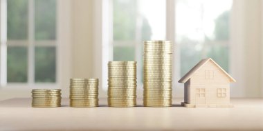 Ahşap bir model evin yanında artan madeni para destelerinin görsel bir temsili, parlak bir pencere arkaplanına karşı kurulmuş gayrimenkul yatırımları için artan tasarruf kavramının sembolü.