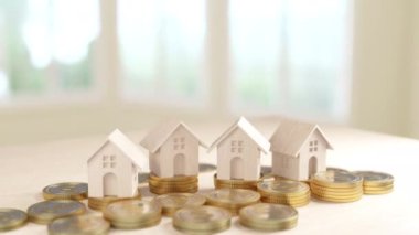 Bu resimde, artan madeni para yığınlarına yerleştirilmiş çoklu ahşap ev modelleri, doğal ışık ayarı ile vurgulanan gayrimenkul yatırımlarındaki büyüme kavramını temsil ediyor..