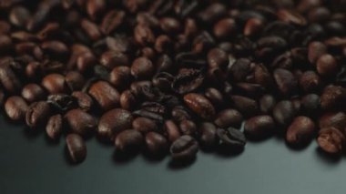 Pürüzsüz bir yüzeye yayılmış bir yığın kavrulmuş kahve çekirdeğinin yakın çekim görüntüsü zengin dokularını ön plana çıkarıyor..