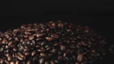 Koyu bir arka planda kavrulmuş kahve çekirdekleri yığınının yakın görüntüsü zengin dokusunu ve rengini gözler önüne seriyor..