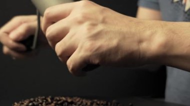 Kahve çekirdeklerini öğütmek için elle öğütücü kullanan ellerin yakın çekimi, kahve hazırlama sürecinin ve dokunsal deneyiminin vurgulanması.