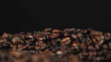 Koyu bir arka planda kavrulmuş kahve çekirdekleri yığınının yakın görüntüsü zengin dokusunu ve rengini gözler önüne seriyor..