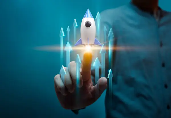 Bir kişinin yukarı doğru ok atarak sanal bir rokete dokunuşunu gösteren bir resim, bir girişimin başlamasını ve büyümesini sembolize ediyor. Girişimcilik ve yenilik temaları için ideal.